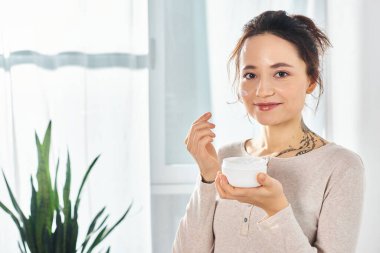 Elinde krema kavanozu tutan şık, esmer bir kadın, bir anlık rahatlama ve hoşgörünün tadını çıkarıyor..