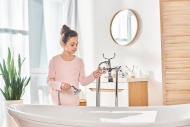 A brunette girl luxuriates in a bathtub, diligently washing her hands in the modern bathroom. clipart