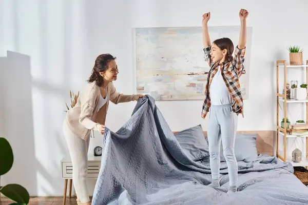 mother and daughter, standing on a bed with a blue blanket, sharing quality time together.