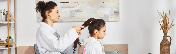 一位黑发母亲穿着白色浴袍坐在卧室的床上 温柔地梳理着小女孩的头发 — 图库照片