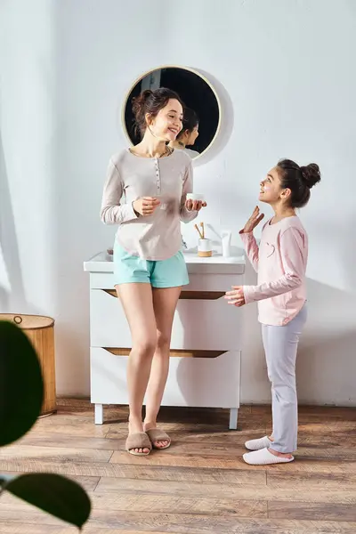 一个黑发女人站在她十几岁的女儿旁边 在一个现代化的浴室里轻轻地涂奶油 — 图库照片