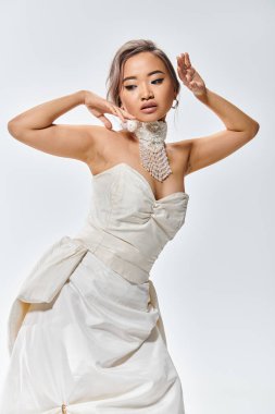 elegant asian woman in white grace dress posing with hands near face and looking to down clipart