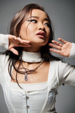 portrait of charming asian woman with heavy makeup posing with hands against grey background clipart