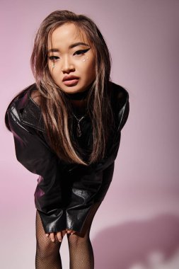 asian young girl in black leather outfit with heavy makeup leaning forward on lilac background clipart