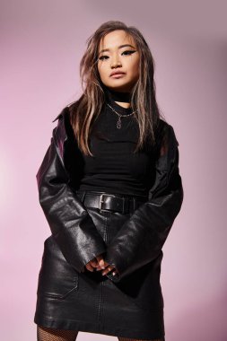 lovely asian young woman in black leather outfit posing against lilac background clipart