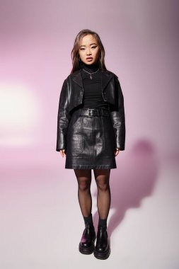 attractive asian woman in black leather outfit with heavy makeup standing on lilac background clipart