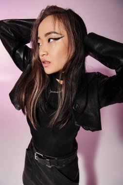 charming asian young woman in leather outfit putting hands behind head and looking to up clipart
