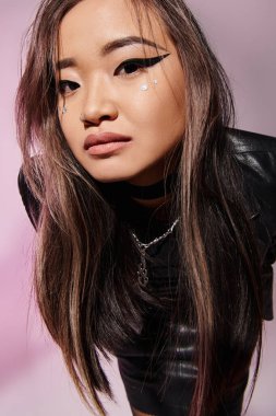 Ağır makyajlı sevimli Asyalı kızın, leylak arka planına doğru eğildiği yakın plan.