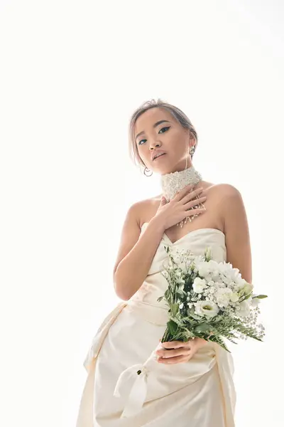 魅力的なアジアの女性は白いネックレスに触れ 光の背景に花束を保持します — ストック写真
