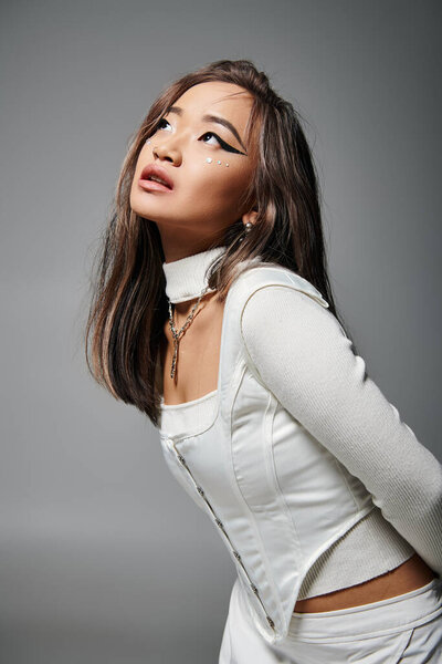 alluring asian woman in stylish outfit with daring makeup sideways leaning forward and looking to up
