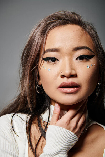 close up of attractive asian woman in her 20s with outrageous makeup against grey background