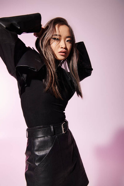 очаровательная молодая женщина в черной кожаной одежде позирует с руками в сторону на сиреневом фоне