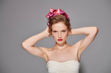 Young woman exuding classic beauty poses in studio wearing white dress with pink bow on head. clipart