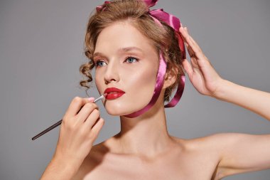 A young woman in a studio setting applies lipstick to her lips, focusing on enhancing her natural beauty. clipart