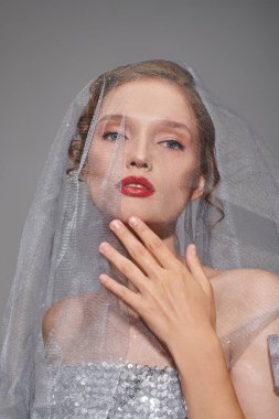 A young woman exuding classic beauty, wearing a veil and vibrant red lipstick in a studio setting on a grey background. clipart