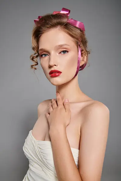 若い女性は 彼女が穏やかなスタジオの設定で彼女の頭にピンクの弓で白いドレスでポーズするように古典的な美しさを排除します — ストック写真