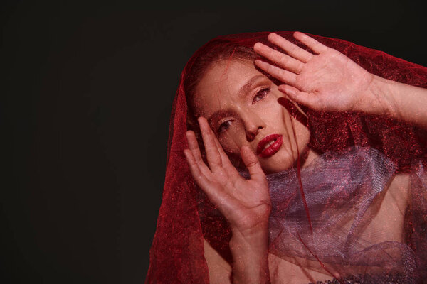 Молодая женщина излучает классическую красоту, позируя с вуалью, покрывающей ее лицо в студии на черном фоне.