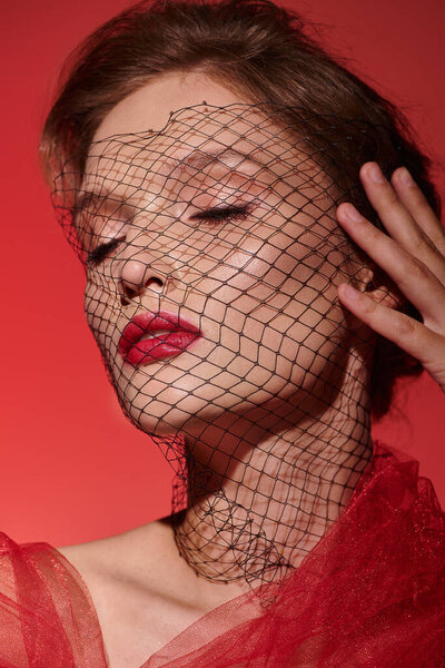 Молодая женщина, излучающая классическую красоту в потрясающем красном платье, с вуалью, изящно покрывающей ее голову.