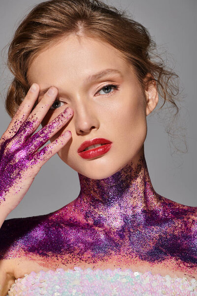 A young woman with classic beauty gracefully holds her face in a studio setting, showcasing elegance and sophistication.