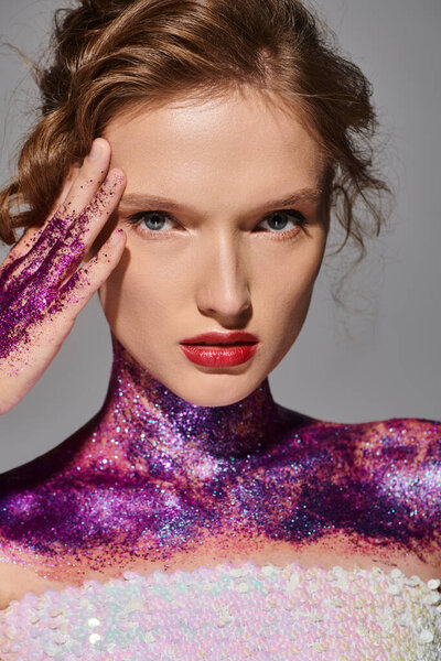 A young woman with classic beauty poses in a studio, her body sparkling with purple and pink glitter.