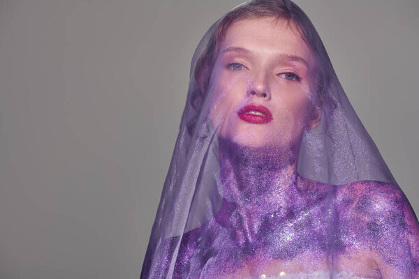 Молодая женщина позирует в студии, излучая классическую красоту, надевая серую вуаль на голову.
