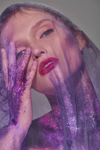 Молодая женщина с классической красотой стоит в студии, нежно прижав руки к лицу в момент уязвимости и элегантности.