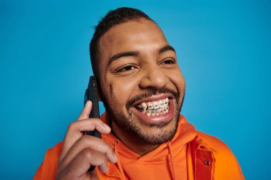 Neşeli Afro-Amerikan 'ın yakın çekimleri mavi arka planda akıllı telefondan arıyor.