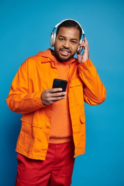 Yakışıklı Afro-Amerikan kulaklıklı adam akıllı telefonuyla müzik dinliyor ve kameraya bakıyor.