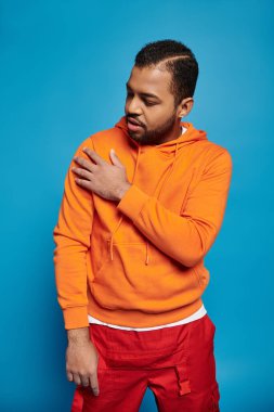 Yakışıklı Afro-Amerikan adam canlı kıyafetli ve mavi arka planda omuz arıyor.
