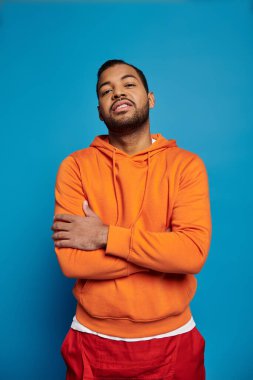 Kendine güvenen Afro-Amerikan bir adam mavi arka planda çapraz silahlarla poz veriyor.