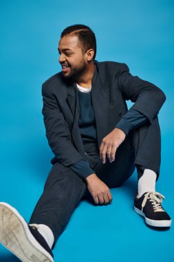 Yakışıklı Afro-Amerikan adam bacağı bükülmüş ve mavi arka planda yer almak istiyor.