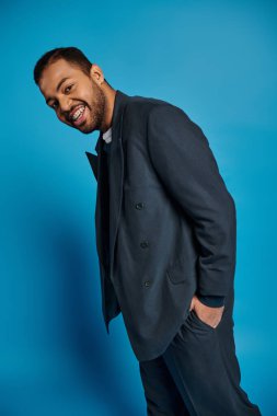 cheerful african american young man in dark blue outfit standing to sideways with hand in pocket clipart