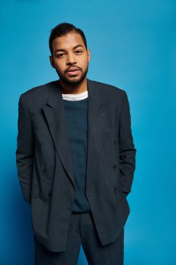 Koyu mavi kıyafetli çekici Afro-Amerikan genç adam elleri ceplerinde kameraya bakıyor.