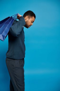 african american man in dark blue outfit looking to down and holding shopping bags over shoulder clipart
