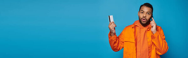 banner of african american young guy calling in smartphone with credit card on blue background