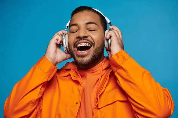 Radostný Africký Američan Oranžovém Kostýmu Poslouchající Hudbu Držící Rukama Sluchátkách — Stock fotografie