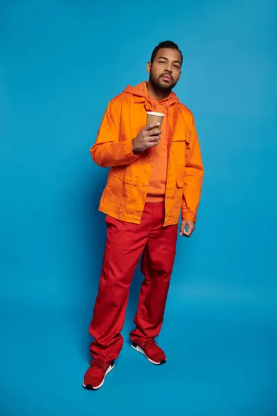 Afrykański Amerykanin Pomarańczowym Stroju Stojący Papierowym Kubkiem Dłoni Niebieskim Tle — Zdjęcie stockowe