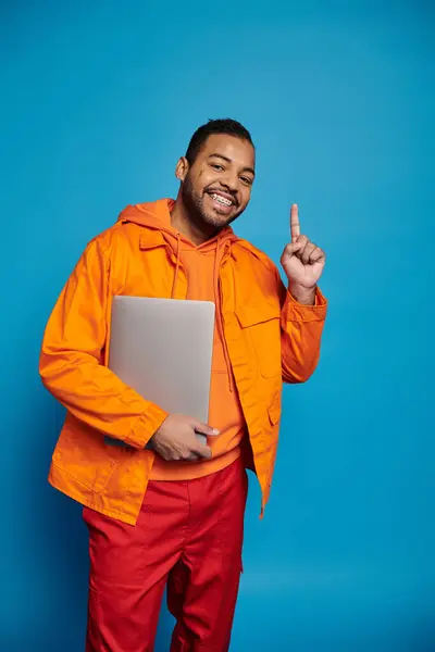 Happy African American Man Orange Outfit Posing Laptop Putting Finger — Fotografia de Stock