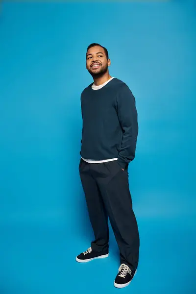 stock image happy african american man in dark outfit standing with hands in pockets and looking to up