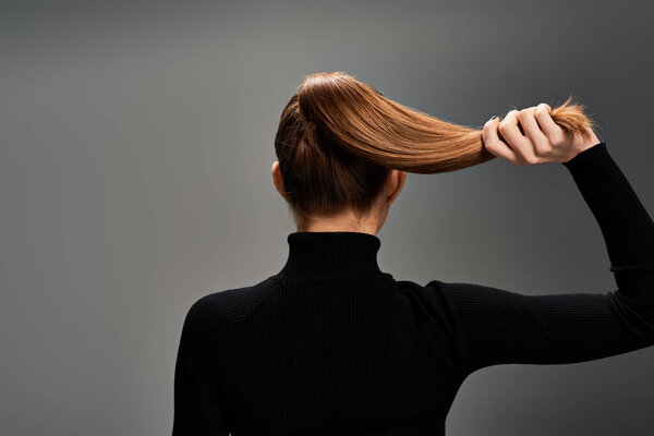 Back view of young stylish woman with long hair elegantly styled in a ponytail, exuding grace and confidence.