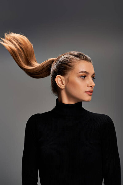 A young, appealing woman with long hair styled in a ponytail, exudes elegance and confidence.