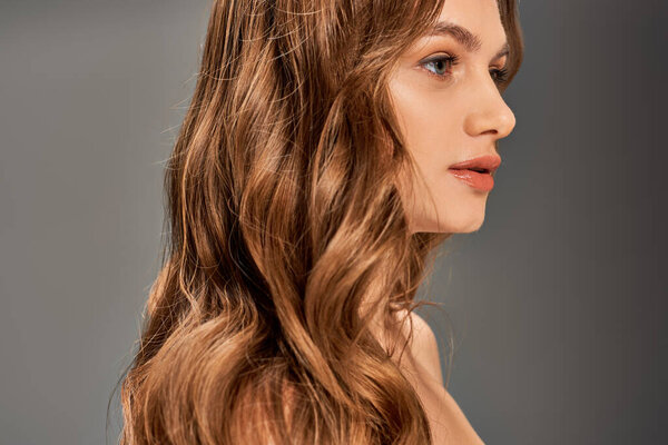 Молодая женщина с длинными волосами задумчиво смотрит прочь, ее волнистые замки каскадом вокруг нее.