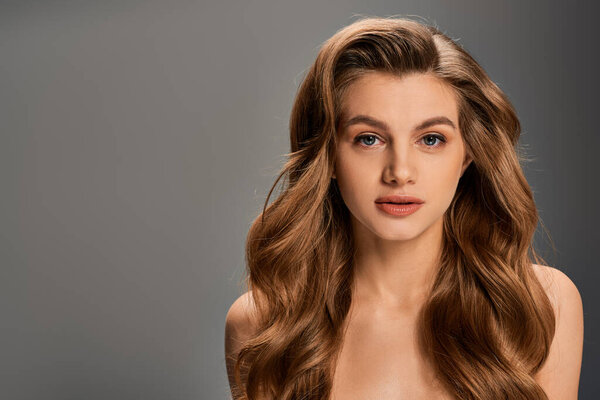 Молодая, красивая женщина безмятежно смотрит своими длинными волнистыми волосами, каскадами качающимися по ее плечам.