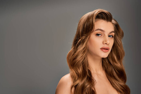 Молодая красивая женщина с длинными волнистыми волосами элегантно позирует на сером фоне