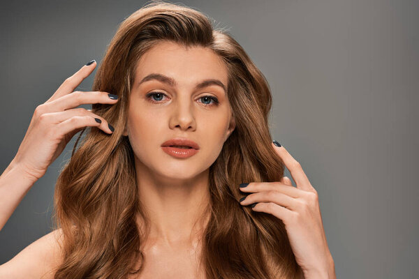 Молодая женщина с длинными коричневыми волнистыми волосами подносит руки к голове в момент созерцания.