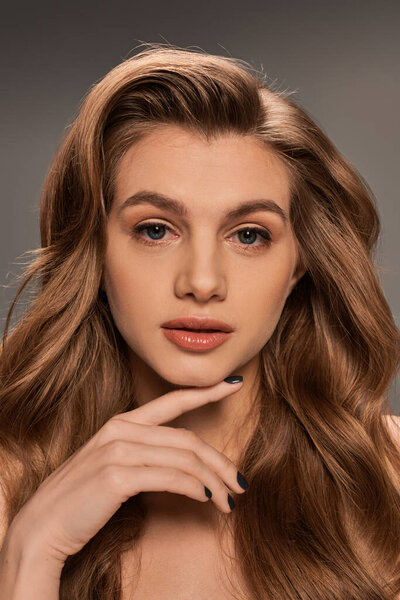 Молодая, красивая женщина с длинными волнистыми волосами изящно позирует перед камерой.