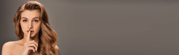 A young woman with long wavy hair holding her finger to her mouth in a secretive gesture, banner