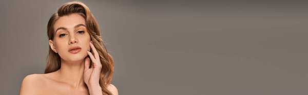 A young woman with long wavy hair gently rests her hand on her face, displaying a moment of deep contemplation.