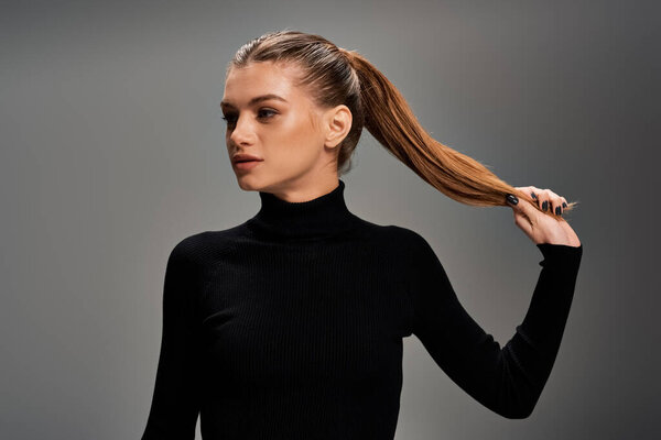 Молодая, красивая женщина с длинными волосами, стилизованная под хвост, в черном топе.