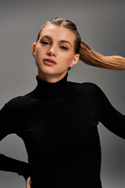 Молодая женщина с длинными волосами уверенно стоит с руками на бедре